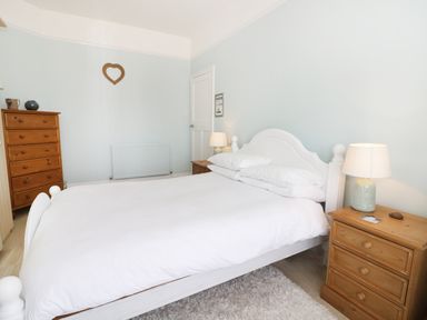 A bedroom with a white bed flanked by wooden bedside tables and a chest of drawers at Number Fifteen in Withernsea