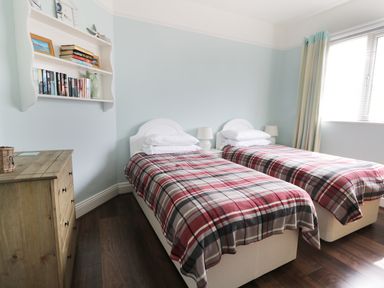 A bedroom with two single beds with plaid blankets a wooden dresser and a wall-mounted bookshelf at Number Fifteen in Withernsea