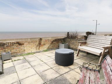 A paved outdoor patio area with wooden benches and a round black table near a brick wall by the sea