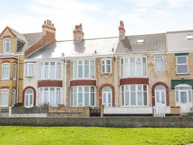 A row of terraced houses with white framed windows and front doors behind low walls with green grass in front at Number Fifteen in Withernsea