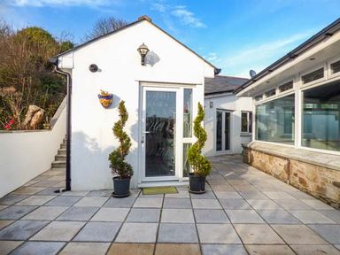 An outdoor patio area with tiled flooring two spiral-shaped potted plants a white building with glass doors and windows at Chapel Green Studio Polgooth near St Austell