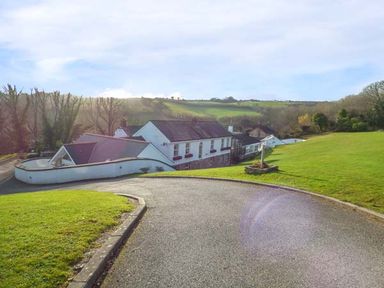 A curved paved driveway leading to a white house with multiple sections surrounded by grass and trees at Chapel Green Studio in Polgooth near St Austell