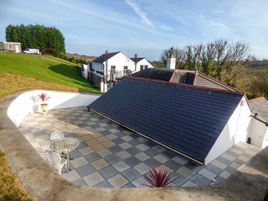 A tiled outdoor patio area with a table and two chairs beside a building roof at Chapel Green Studio in Polgooth near St Austell