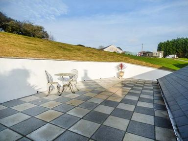 An outdoor patio with a checkered tile floor a small table and two chairs and a potted plant on a slope at Chapel Green Studio Polgooth near St Austell