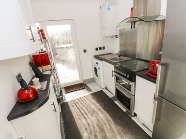 A kitchen with white cabinets a red kettle and toaster a washing machine and stainless steel appliances at Chapel Green Studio in Polgooth near St Austell