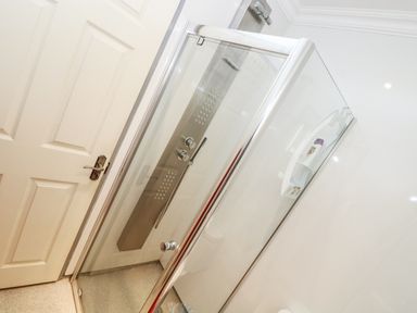 A shower enclosure with glass doors and wall controls next to a closed white door at Chapel Green Studio in Polgooth near St Austell