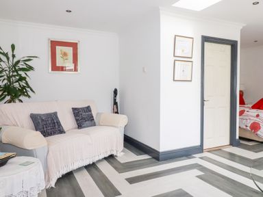 A living room with a sofa a plant framed pictures and a door leading to a bedroom at Chapel Green Studio Polgooth near St Austell