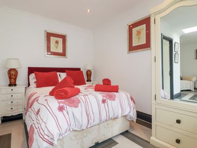 A bedroom with a double bed with red pillows and towels bedside tables with lamps and framed flower pictures on walls at Chapel Green Studio in Polgooth near St Austell