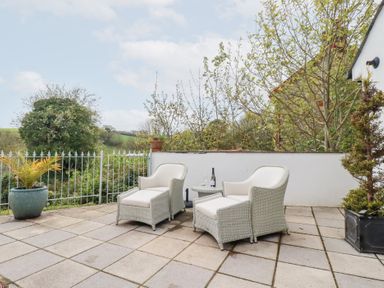 An outdoor patio with two white armchairs a small round table and potted plants at Chapel Green Studio Polgooth near St Austell