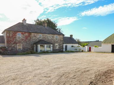 An exterior view of a stone house with attached white buildings and a gravel yard at Ballintlea Ballintlea near Dungarvan County Waterford
