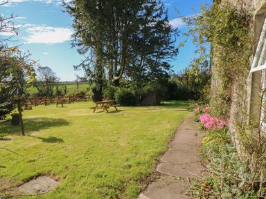 A garden with grass, picnic tables, a bird feeder, and a path next to a house with flowers at Ballintlea in Ballintlea near Dungarvan County Waterford