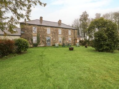 A stone house with a blue door and windows in a green yard with chairs a picnic table and trees at Ballintlea near Dungarvan County Waterford