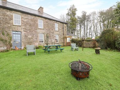 A backyard with green grass a fire pit wooden chairs a picnic table and a stone house at Ballintlea near Dungarvan County Waterford