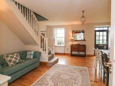 A living room with a green sofa near stairs a wooden sideboard under a mirror and a dining table with chairs at Ballintlea in Ballintlea near Dungarvan County Waterford