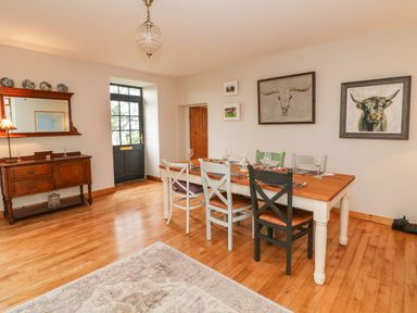A dining room with a wooden table and mixed chairs a sideboard with a mirror and decorative plates on top and animal artwork on the walls at Ballintlea near Dungarvan County Waterford