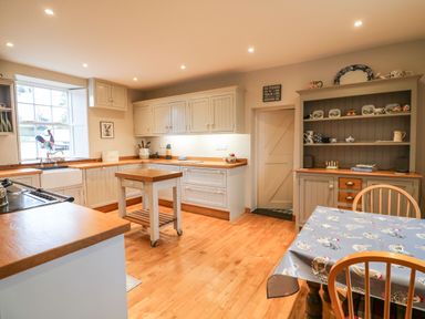 A kitchen with wooden countertops white cabinets a small island a table with chairs and a cupboard with dishes at Ballintlea Ballintlea near Dungarvan County Waterford