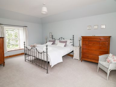 A bedroom with a metal bed frame white bedding wooden chest of drawers and a wicker chair next to a window at Ballintlea near Dungarvan County Waterford