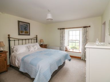 A bedroom with a bed with blue quilt nightstands with lamps a window with curtains and a white dresser at Ballintlea in Ballintlea near Dungarvan County Waterford