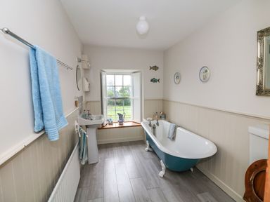 A bathroom with a clawfoot bathtub a pedestal sink a window with a wooden sill and a blue towel on a rack at Ballintlea near Dungarvan County Waterford