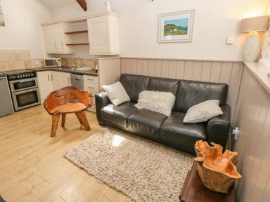 A living area with a black leather sofa and wooden chair next to a kitchen with white cabinets at The Barn at Waunlippa in Narberth