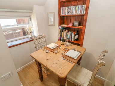 A small dining table set for two with plates glasses and cutlery next to a bookshelf with books and bottles at The Barn at Waunlippa Narberth