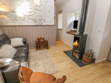 A living room with a black leather sofa a wooden chair small nested tables a wood burning stove and a small window with a tv at The Barn at Waunlippa Narberth