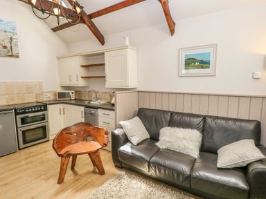 A living room with a black leather sofa and wooden chair next to a kitchen with cabinets and appliances at The Barn at Waunlippa Narberth