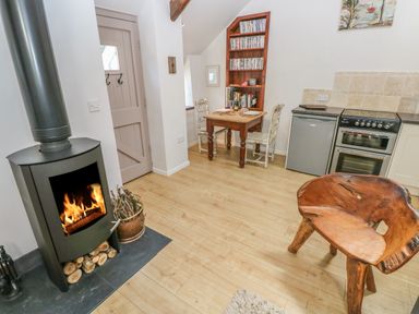 A small kitchen and dining area with a wood burning stove a wooden table with two chairs and a rustic wooden chair at The Barn at Waunlippa in Narberth