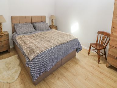 A bedroom with a bed with striped bedding and a fur cover a wooden chair two bedside tables with lamps and a wooden dresser at The Barn at Waunlippa Narberth