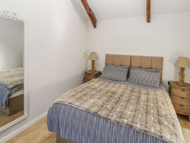 A bedroom with a bed striped bedding two bedside tables with lamps and a wall mirror at The Barn at Waunlippa in Narberth