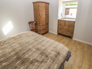 A bedroom with a bed covered with a fur blanket wooden wardrobe wooden chair and wooden dresser under a window at The Barn at Waunlippa in Narberth