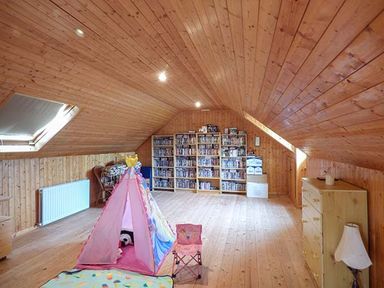 An attic room with wooden walls and ceiling a pink children's play tent a small chair bookshelves filled with books and a chest of drawers with a lamp at The Sanctuary in Killavullen near Mallow