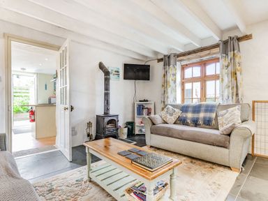 A living room with two sofas a coffee table a wood-burning stove a wall-mounted TV and a window with curtains at Victoria Cottage in St Newlyn East near Newquay