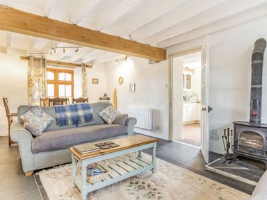 A living room with a sofa coffee table wood stove and dining area at Victoria Cottage St Newlyn East near Newquay