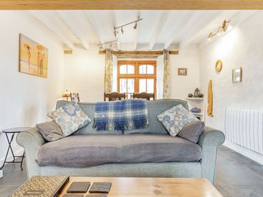 A living room with a sofa a coffee table paintings on the wall and a wooden window at Victoria Cottage in St Newlyn East near Newquay