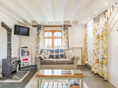 A living room with a wood stove and sofa under a window with floral curtains at Victoria Cottage in St Newlyn East near Newquay