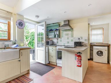 A kitchen with a sink, stove, microwave, toaster, washing machine, open door to a garden and a fire extinguisher at Victoria Cottage in St Newlyn East near Newquay