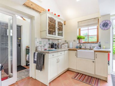 A kitchen with white cabinetry a window above the sink and a wall clock at Victoria Cottage in St Newlyn East near Newquay