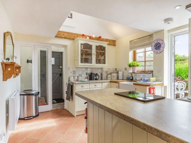 A kitchen with a countertop island a sink under a window and a door leading outside at Victoria Cottage in St Newlyn East near Newquay