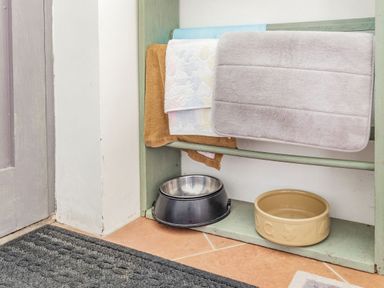 Two pet bowls and towels hanging on a wooden rack on a tiled floor at Victoria Cottage in St Newlyn East near Newquay