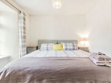 A bedroom with a double bed two bedside tables a lamp folded towels and a window with plaid curtains at Victoria Cottage in St Newlyn East near Newquay