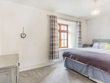 A bedroom with a bed next to a window with curtains and a chest of drawers on carpeted floor at Victoria Cottage in St Newlyn East near Newquay