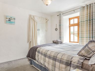 A bedroom with a bed covered in plaid bedding next to a window with plaid curtains at Victoria Cottage in St Newlyn East near Newquay