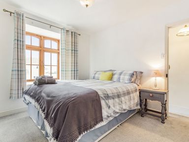 A bedroom with a large bed next to a window and a bedside table with a lamp at Victoria Cottage in St Newlyn East near Newquay