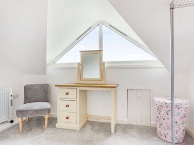A corner of a room with a vanity table mirror a gray chair and a floral laundry basket at Victoria Cottage in St Newlyn East near Newquay