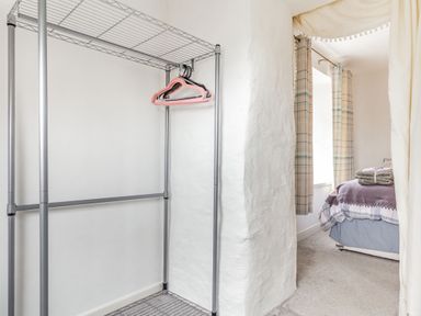 A closet area with a metal clothing rack and hangers next to a bedroom with a bed and curtains at Victoria Cottage in St Newlyn East near Newquay
