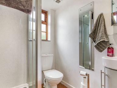 A bathroom with a toilet, glass shower enclosure, small sink, mirror, towel, and window at Victoria Cottage in St Newlyn East near Newquay