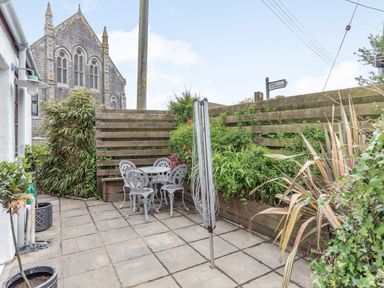A small paved patio with metal table and chairs surrounded by plants and a wooden fence at Victoria Cottage in St Newlyn East near Newquay
