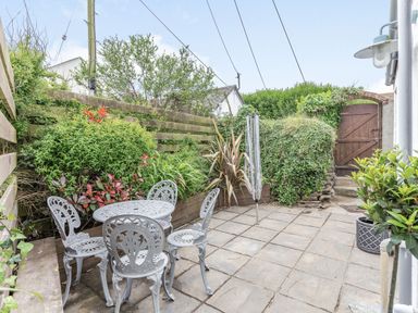 A small paved patio with metal table and chairs surrounded by plants and a wooden gate at Victoria Cottage in St Newlyn East near Newquay