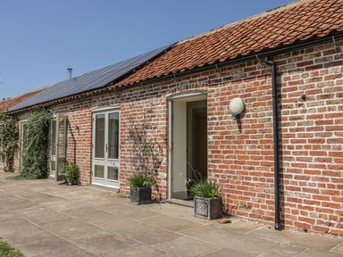 A brick building with tiled roof solar panels and plants in pots on the patio at Cow Byre in Malton